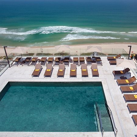 Windsor Marapendi Hotel Rio de Janeiro Exteriér fotografie The photo shows a rooftop area with a swimming pool and several lounge chairs arranged around it. The pool has a clear blue surface, and the lounge chairs are positioned in a neat row, some with yellow cushions. In the background, you can see a beaut