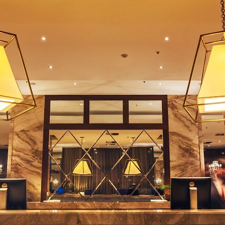 Windsor Marapendi Hotel Rio de Janeiro Exteriér fotografie The photo shows a hotel lobby or reception area. There are large geometric light fixtures hanging from the ceiling, providing a warm glow to the space. The reception desk is made of a polished material, likely marble, with decorative elements and two