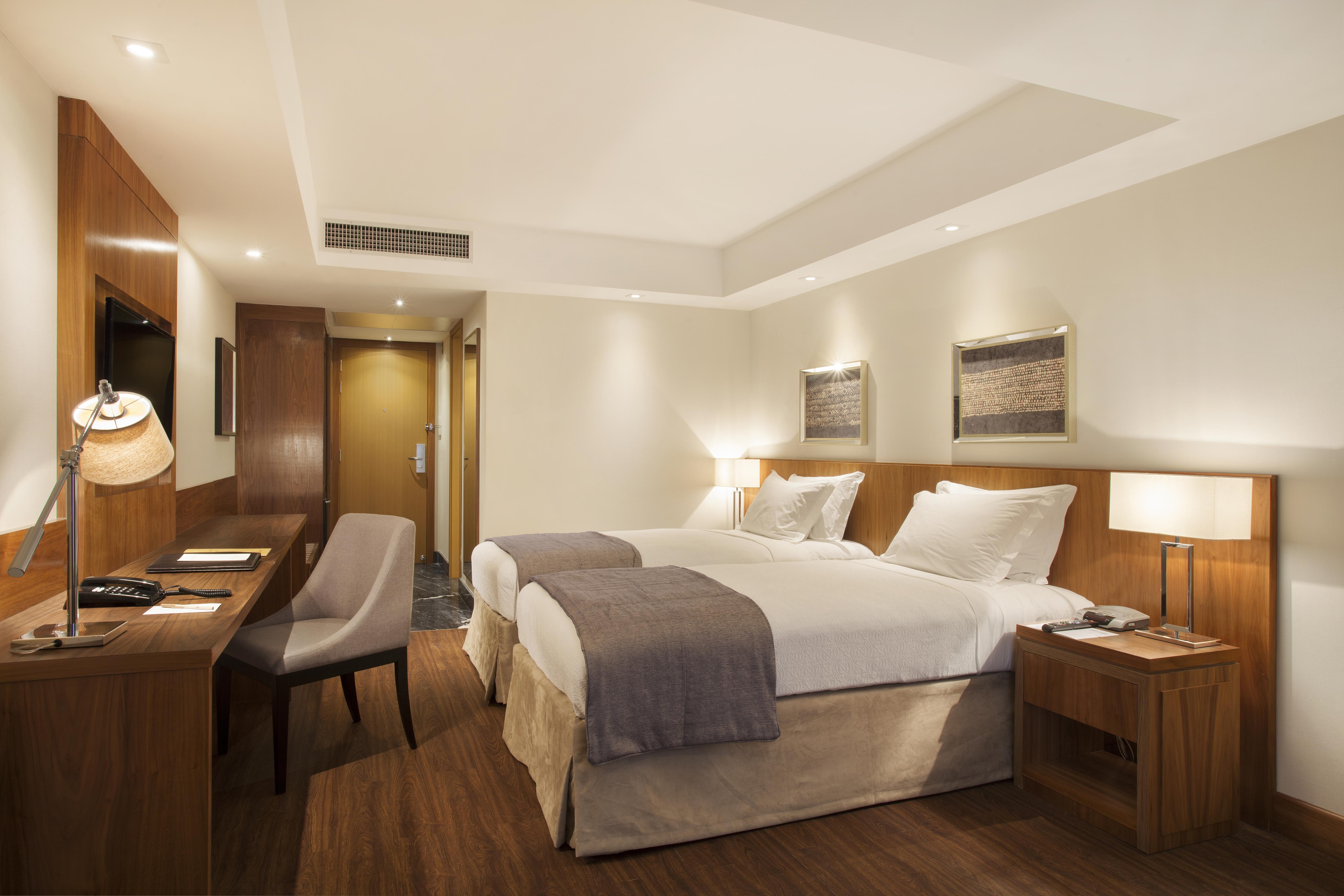 Windsor Marapendi Hotel Rio de Janeiro Exteriér fotografie The photo displays a modern hotel room featuring two twin beds with crisp white linens and gray throw blankets. The room has a clean and minimalist design, with wooden accents, including a bedside table and a desk. To the left, there's a small desk a
